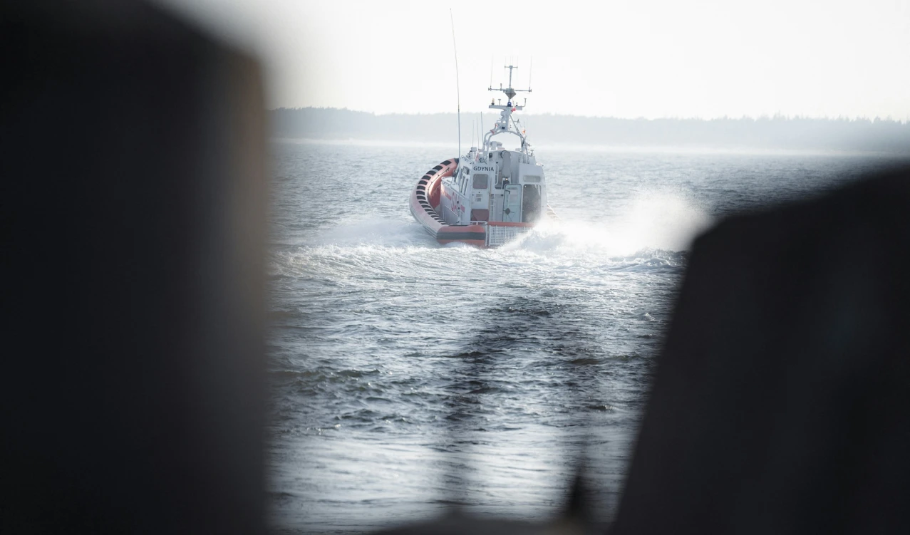Red and white rescue boat speeding across open water, leaving a foamy wake behind it.