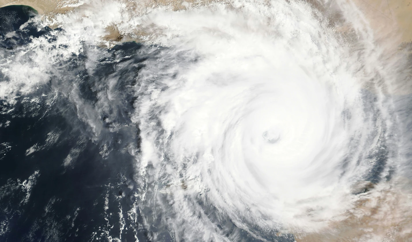 Satellite image of a large tropical cyclone over the ocean, with dense spiral cloud bands surrounding a visible eye near the coast.
